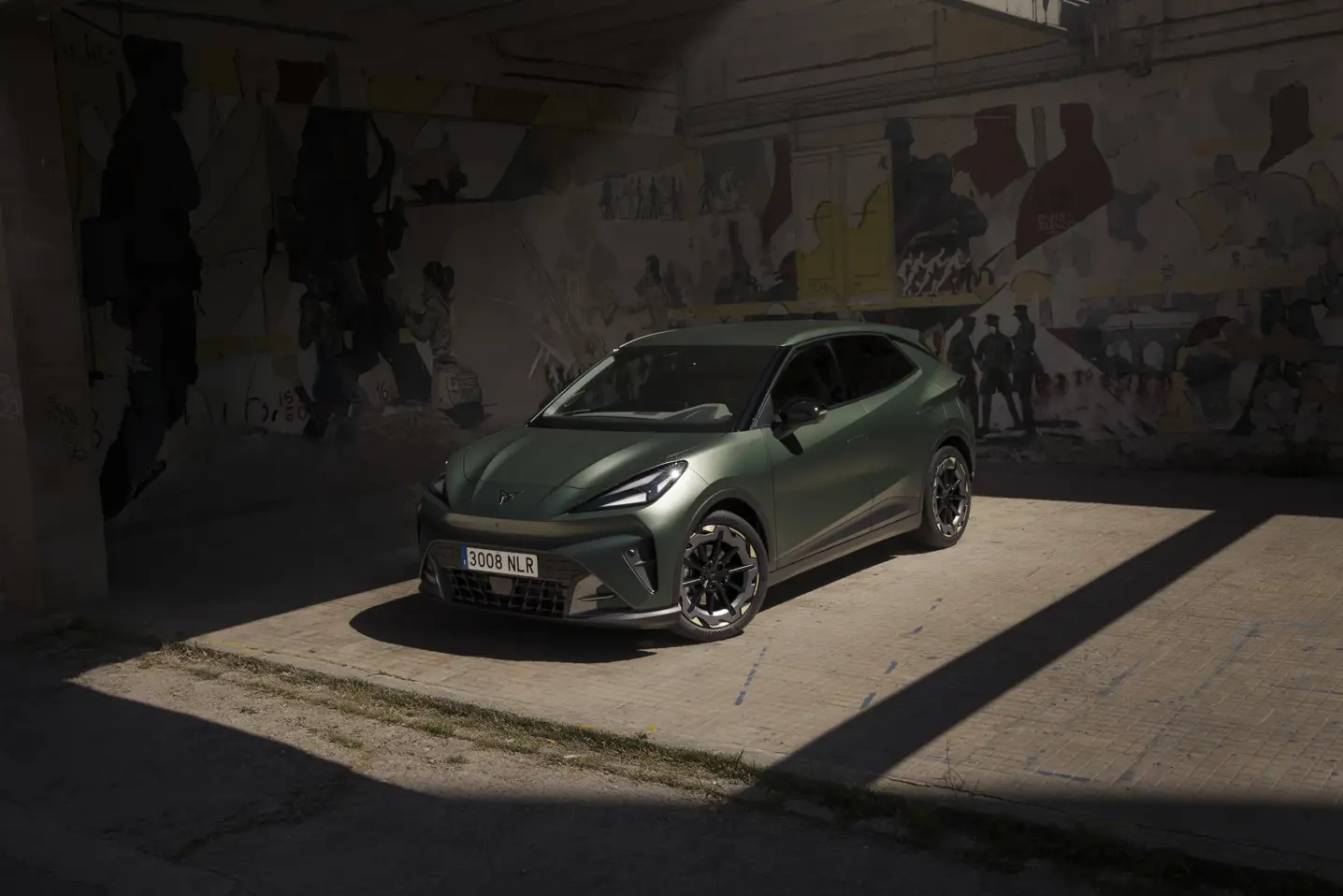En grøn CUPRA Raval elbil holder parkeret i en skyggefuld, rå betonhal med graffitimalede vægge.